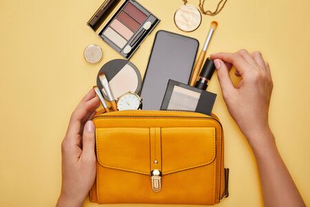 cropped view of woman holding lipstick near bag isolated on yellowの写真素材