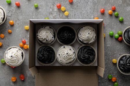 top view of delicious Halloween cupcakes in box near scattered colorful bonbons on concrete grey surfaceの写真素材