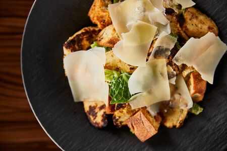 tasty Caesar salad with Parmesan slices served on plate on wooden tableの写真素材
