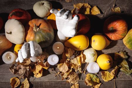 top view of dry foliage, burning candles, ripe pumpkin and decorative hands on wooden rustic tableの写真素材