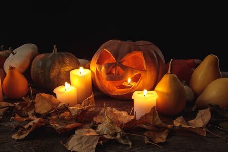 dry foliage, burning candles and Halloween carved pumpkin on wooden rustic table isolated on blackの写真素材