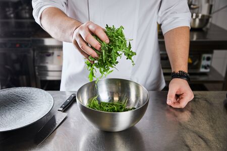 cropped view of chef cooking salad with arugula at kitchen in restaurantの写真素材