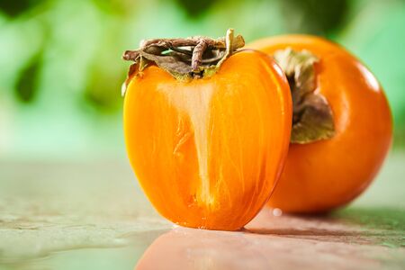 selective focus of whole and cut persimmons on marble surfaceの写真素材