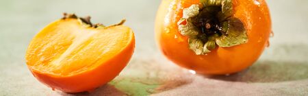 panoramic shot of whole and cut persimmons on marble surfaceの写真素材