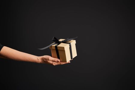cropped view of woman holding cardboard gift box with ribbon isolated on black, black Friday conceptの写真素材