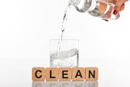 cropped view of woman pouring water from bottle in glass near cubes with clean lettering isolated on...