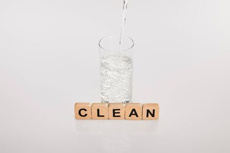 clear fresh water pouring in glass near cubes with clean lettering on grey backgroundの写真素材