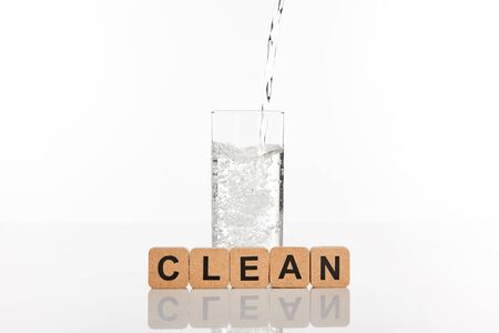 clear fresh water pouring in glass near cubes with clean lettering isolated on whiteの写真素材