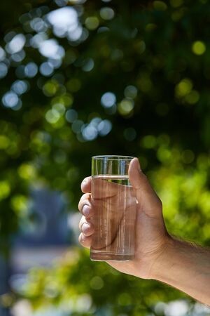 cropped view of man holding glass with clear fresh water outdoor