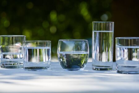 clear fresh water in transparent glasses in sunlight on wooden table