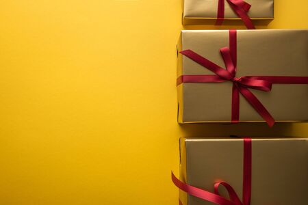 top view of golden gift boxes with red ribbons on yellow background with copy space