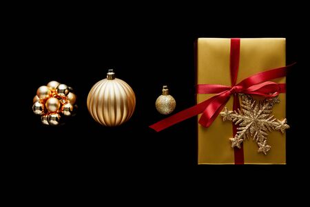 flat lay with shiny golden Christmas gift with red ribbon and snowflake near baubles isolated on...