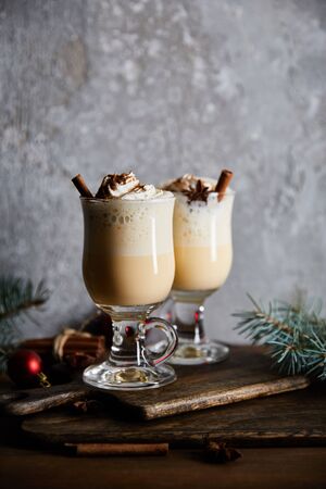 traditional eggnog cocktail with whipped cream and cinnamon on cutting board near spruce branches on grey stone backgroundの写真素材