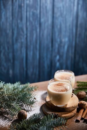 flavored eggnog cocktail, spruce branches, cinnamon sticks and walnuts on wooden table covered with sugar powder on blue textured backgroundの写真素材