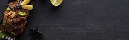 top view of meat thai noodles near chopsticks and lime on wooden grey surface, panoramic shot