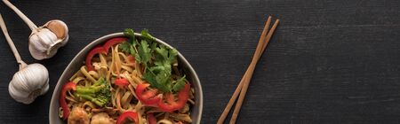 top view of tasty spicy thai noodles with garlic near chopsticks on wooden grey surface, panoramic...