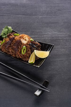 meat delicious spicy thai noodles near chopsticks on wooden grey surface