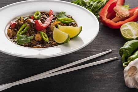 vegetable delicious spicy thai noodles near chopsticks and ingredients on wooden grey surface