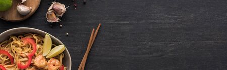top view of tasty spicy thai noodles with garlic and shrimps near chopsticks on wooden grey surface,...