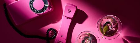 Top view of vintage telephone and two martini cocktails on pink background, panoramic shot