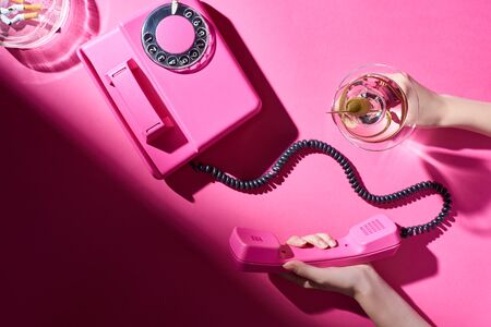 Cropped view of woman holding cocktail and telephone handset beside astray with cigarette butts on...