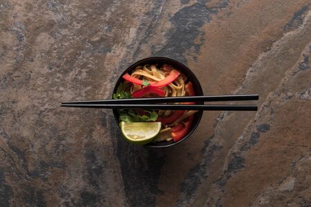 top view of delicious spicy thai noodles with chopsticks in bowl on stone surfaceの写真素材