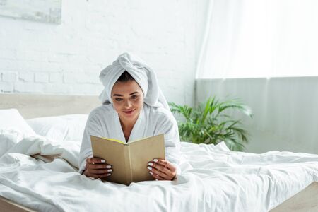 attractive woman in towel and bathrobe reading book at morningの写真素材