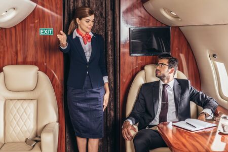 flight attendant showing gestures to handsome businessman in suit in private plane
