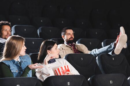 multicultural friends with popcorn looking at ill-mannered man in cinema