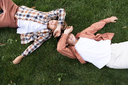 top view of two smiling brothers covering eyes with hands while lying on grassの写真素材