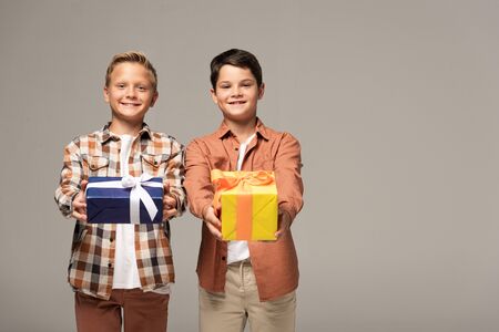 two happy brothers holding blue and yellow gift boxes isolated on grey