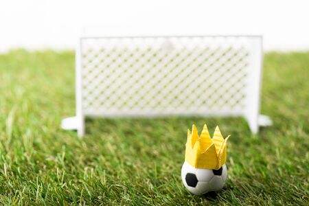 selective focus of toy football gates and ball with paper crown on green grass isolated on white, sports betting conceptの写真素材