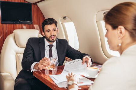 businessman with glass showing contract to businesswoman in private planeの写真素材