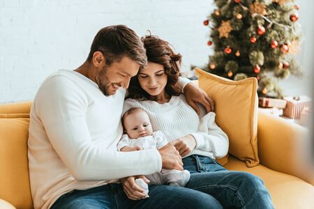 happy parents holding adorable baby while sitting on yellow sofa