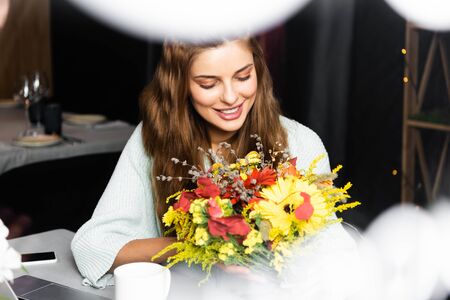 cheerful redhead woman with bouquet of autumn flowers in cafeの写真素材