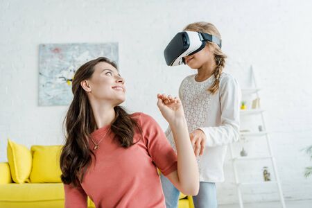 happy babysitter looking at cheerful kid in virtual reality headsetの写真素材