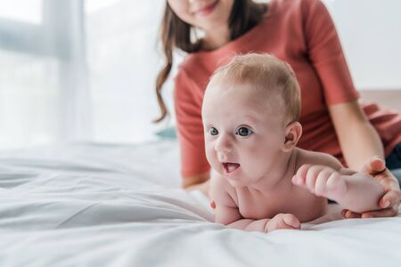 cropped view of happy woman touching baby daughter lying on bed at homeの写真素材