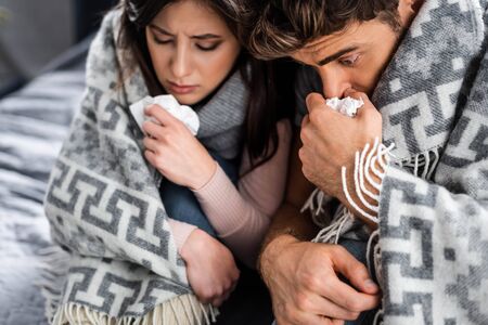 selective focus of sick girlfriend and boyfriend covered with blanket and holding napkins