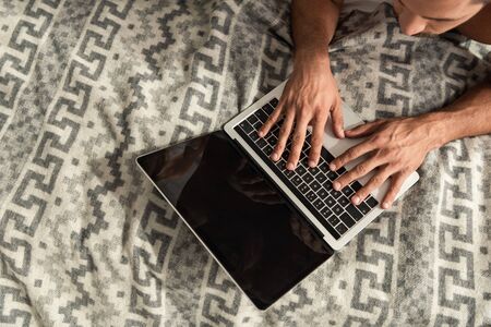 top view of man lying on bed and using laptop with blank screenの写真素材