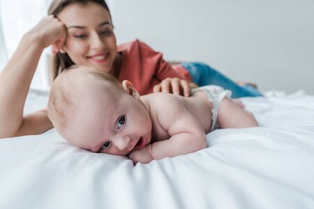 selective focus of cute infant near cheerful mother in bedroomの写真素材