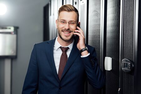 cheerful businessman in glasses talking on smartphone in server room