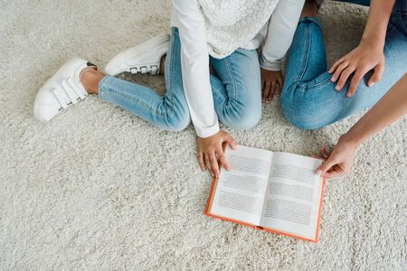 top view of babysitter sitting on carpet with kid near book