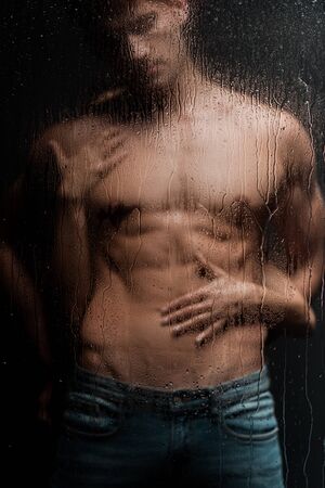 passionate woman hugging shirtless man behind wet glassの写真素材