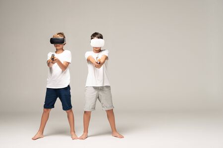 two brothers in vr headsets aiming with toy guns at camera on grey backgroundの写真素材