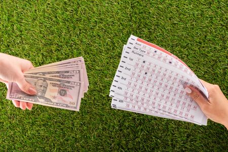 partial view of female hands with dollar banknotes and betting lists on green grass, sports betting conceptの写真素材