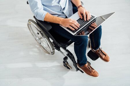 Cropped view of man sitting in wheelchair and using laptop