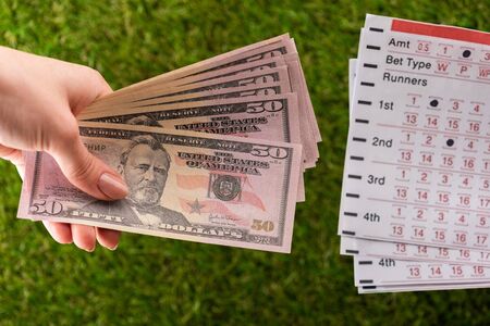 cropped view of woman holding dollar banknotes near betting lists on green grass, sports betting conceptの写真素材