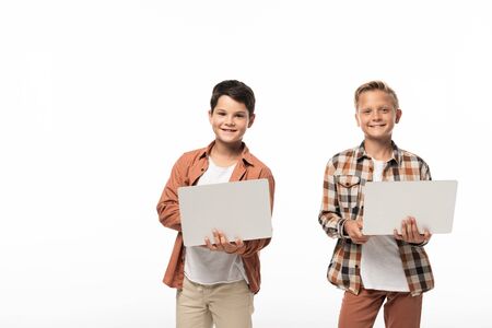 two smiling brothers holding laptops and smiling at camera isolated on whiteの写真素材