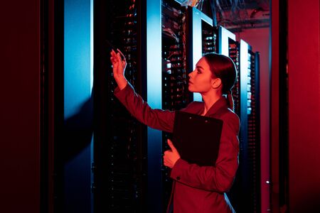 side view of businesswoman holding clipboard and looking at server roomの写真素材