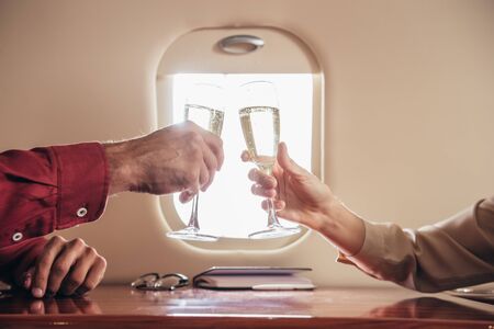 cropped view of boyfriend and girlfriend clinking with champagne glasses in private planeの写真素材